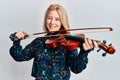 Young blonde woman playing violin winking looking at the camera with sexy expression, cheerful and happy face