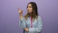 Young blonde woman points assertively against an isolated purple wall in a confident expression Royalty Free Stock Photo