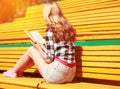 Young blonde woman reading book sitting on the bench in the city park Royalty Free Stock Photo