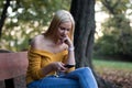 Young blonde woman resting on a bench in the forest, using smartphone Royalty Free Stock Photo