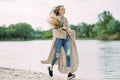 Blonde woman runs along coastline of lake with bouquet in her hands