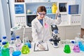 Young blonde woman scientist analysing test tube writing on clipboard at laboratory