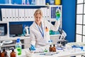 Young blonde woman scientist measuring liquid writing on document at laboratory Royalty Free Stock Photo