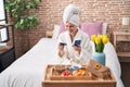 Young blonde woman shopping with smartphone and holding credit card having breakfast at bedroom Royalty Free Stock Photo