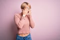 Young blonde woman with short hair wearing casual turtleneck sweater over pink background rubbing eyes for fatigue and headache, Royalty Free Stock Photo