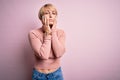 Young blonde woman with short hair wearing casual turtleneck sweater over pink background Tired hands covering face, depression Royalty Free Stock Photo