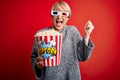 Young blonde woman with short hair wearing 3d movie glasses and eating popcorn at the cinema screaming proud and celebrating Royalty Free Stock Photo