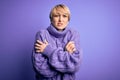Young blonde woman with short hair wearing winter turtleneck sweater over purple background shaking and freezing for winter cold Royalty Free Stock Photo