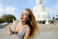 Young blonde woman showing thumbs up, white Buddha statue in Phuket in background.