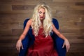 Young blonde woman sits on armchair. Pensive girl in elegant red dress Royalty Free Stock Photo