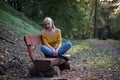 Young blonde woman sitting alone on a wooden bench in the forest, sad and lonely Royalty Free Stock Photo