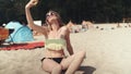 Pretty woman in bikini sitting on the beach and taking a selfie. Royalty Free Stock Photo