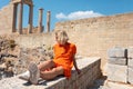 A young blonde woman is sitting and enjoying the view of the coast near the city of Lindos, Greece. Royalty Free Stock Photo