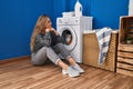 Young blonde woman sitting on the floor waiting for washing machine at laundry room Royalty Free Stock Photo