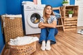 Young blonde woman sitting on the floor waiting for washing machine at laundry room Royalty Free Stock Photo