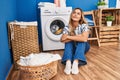 Young blonde woman sitting on the floor waiting for washing machine at laundry room Royalty Free Stock Photo