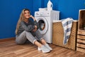 Young blonde woman sitting on the floor waiting for washing machine at laundry room Royalty Free Stock Photo