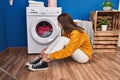 Young blonde woman sitting on floor waiting for washing machine at laundry room Royalty Free Stock Photo