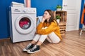 Young blonde woman sitting on floor waiting for washing machine at laundry room Royalty Free Stock Photo