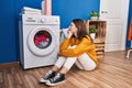 Young blonde woman sitting on floor waiting for washing machine at laundry room Royalty Free Stock Photo