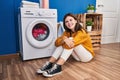 Young blonde woman sitting on floor waiting for washing machine smiling at laundry room Royalty Free Stock Photo
