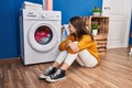 Young blonde woman sitting on floor waiting for washing machine smiling at laundry room Royalty Free Stock Photo