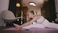 Young blonde woman sitting in half-splices on a yoga mat doing stretching