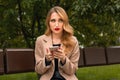 Young blonde woman is sitting on a Park bench and waiting for a phone call from her boyfriend Royalty Free Stock Photo
