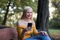 Young blonde woman resting on a bench in the forest, using smartphone Royalty Free Stock Photo