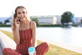 Young blonde woman sitting in riverbank outdoors talking by mobile phone Royalty Free Stock Photo