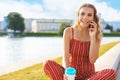 Young blonde woman sitting in riverbank outdoors talking by mobile phone. Royalty Free Stock Photo