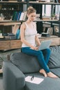 Young blonde woman sitting on sofa and using laptop Royalty Free Stock Photo