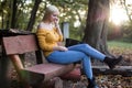 Young blonde woman sitting on a wooden bench in the park, listening to music Royalty Free Stock Photo