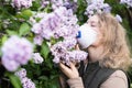 Young blonde woman smells lilac tree blossom through FFP2 respirator. Conceptual image of corona virus quarantine Royalty Free Stock Photo