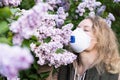 Young blonde woman smells lilac tree blossom through FFP2 respirator. Conceptual image of corona virus quarantine Royalty Free Stock Photo