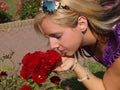 Young blonde woman smells red roses.