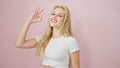 Young blonde woman smiling with ok gestur over isolated pink background