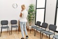 Young blonde woman standing backwards looking clock at waiting room