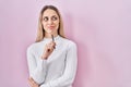 Young blonde woman standing holding pen over pink background smiling looking to the side and staring away thinking Royalty Free Stock Photo