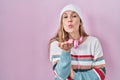 Young blonde woman standing over pink background looking at the camera blowing a kiss with hand on air being lovely and sexy Royalty Free Stock Photo