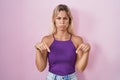 Young blonde woman standing over pink background pointing down looking sad and upset, indicating direction with fingers, unhappy Royalty Free Stock Photo