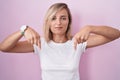 Young blonde woman standing over pink background pointing down looking sad and upset, indicating direction with fingers, unhappy Royalty Free Stock Photo