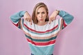 Young blonde woman standing over pink background pointing down looking sad and upset, indicating direction with fingers, unhappy Royalty Free Stock Photo