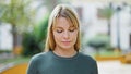 Young blonde woman standing with serious expression looking down at park Royalty Free Stock Photo