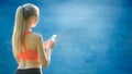 Young blonde woman stands on a blue sea background with a mobile phone. A sporty woman uses a phone near the sea Royalty Free Stock Photo