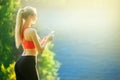 Young blonde woman stands on a blue sea background with a mobile phone. A sporty woman uses a phone near the sea Royalty Free Stock Photo