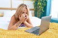 Young blonde woman stressed using laptop lying on bed at bedroom Royalty Free Stock Photo