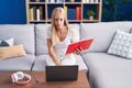 Young blonde woman student sitting on sofa reading book at home Royalty Free Stock Photo