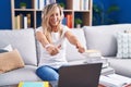 Young blonde woman studying using computer laptop at home approving doing positive gesture with hand, thumbs up smiling and happy Royalty Free Stock Photo