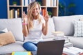 Young blonde woman studying using computer laptop at home gesturing finger crossed smiling with hope and eyes closed